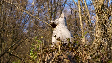 a majestic wolf made of wood is sitting on a strunk in an austrian forest in autumn