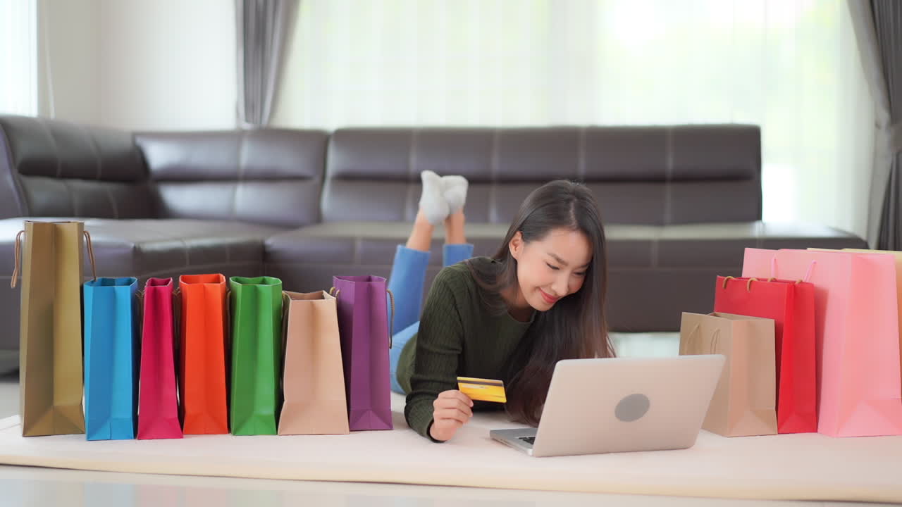 While inputting her credit card number into a laptop a pretty Asian woman enjoys the online shopping experience
