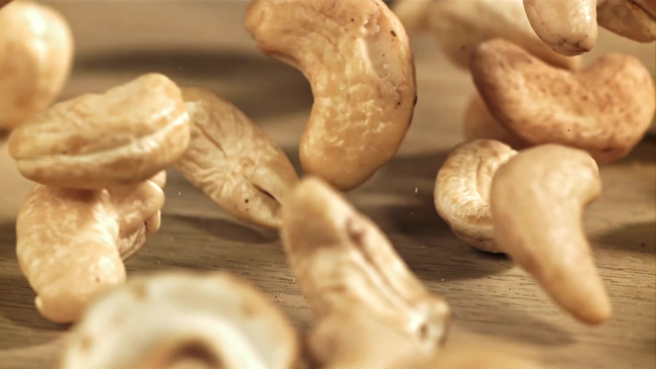 Sakte film av cashewnøtter som faller ned på en treflate.