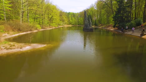 Drone-fast-footage-of-a-lake-in-a-forest-park,-a-beautifully-designed-concrete,-curb-foot-bridge-connecting-the-two-sides-of-the-forest