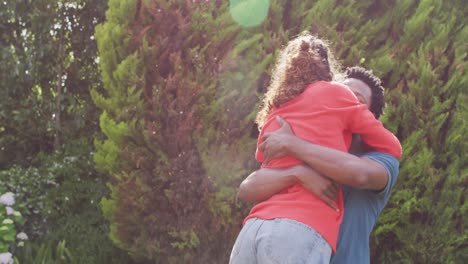 feliz hombre biracial abrazando a su prometida con anillo de compromiso en la mano en el jardín al sol