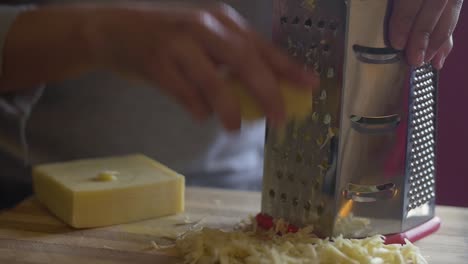 Mano-De-Mujer-Rallando-Queso-En-Una-Tabla-De-Cortar-De-Madera