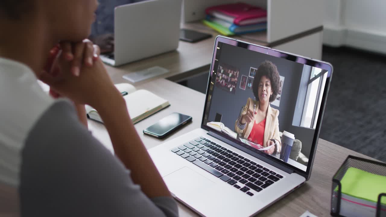 African american businesswoman sitting at desk using laptop having video call with female colleague