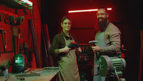 Portrait-of-Caucasian-male-and-female-co-workers-in-aprons-and-goggles-looking-and-smiling-at-camera-in-workshop