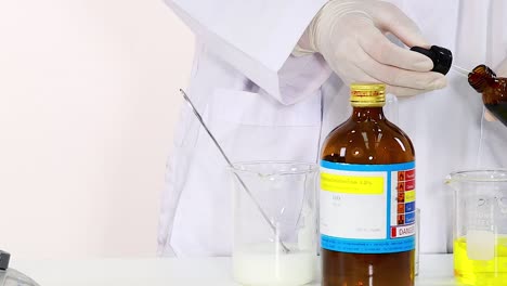 a scientist uses a dropper to mix a yellow solution in a lab setting with glassware.