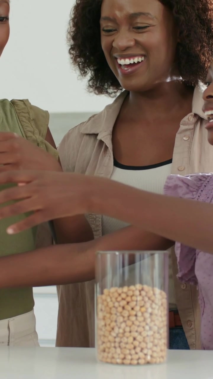 Vertical video: Tipping yellow bag, mother wearing beige guiding girls steadying jar at counter
