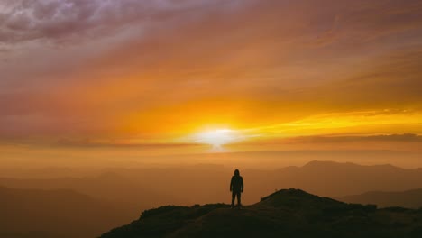 the man standing on a mountain top on the bright sunset background