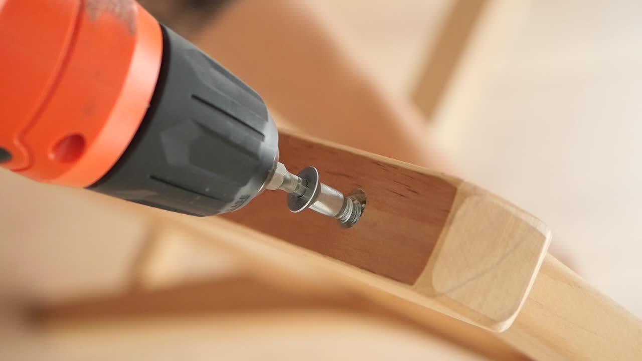 Close-up of a power drill being used to fasten a screw into wood during assembly