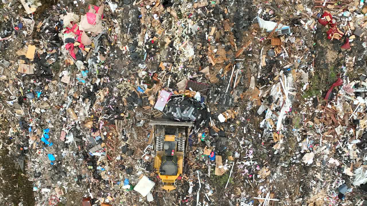 Top down aerial drone view of heavy machinery (Bulldozer) pushing trash in a landfill