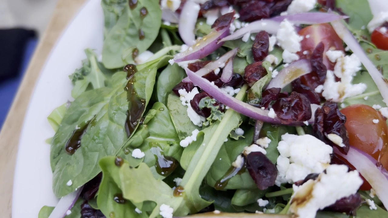 Frisk salat med spinat, rødløk, rosiner og fetaost i nærbilde.