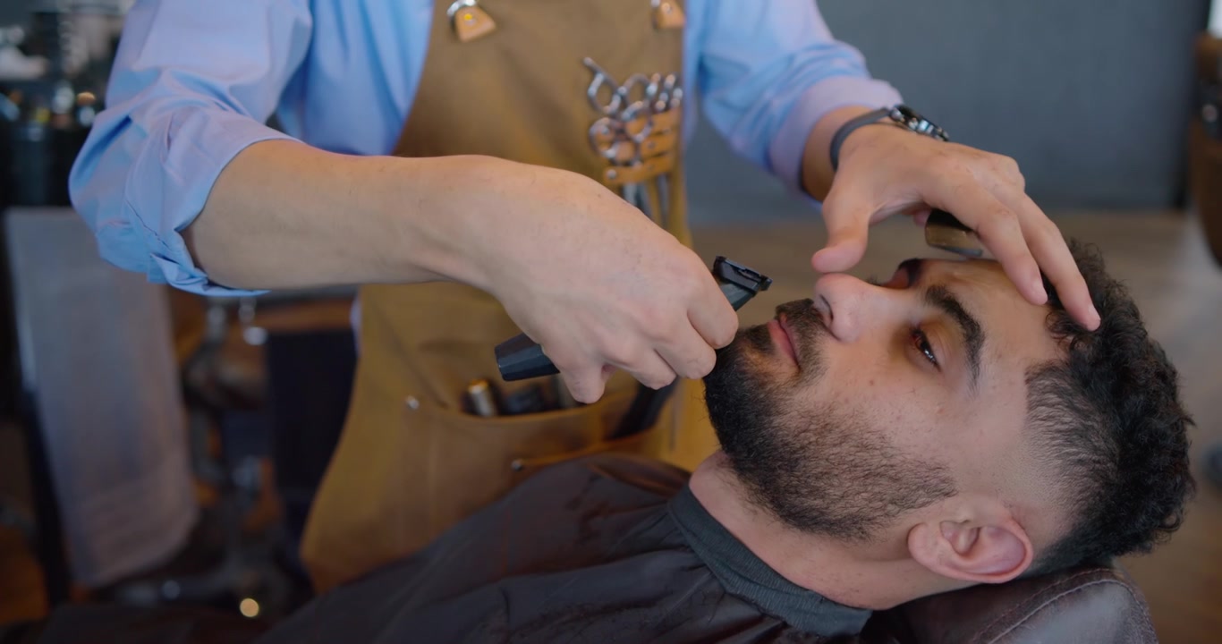 Barbeiro aparando bigode com aparador enquanto cliente reclinado, homens negros, cuidando da aparência na barbearia