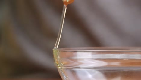 fresh brown egg being cracked on the side of a clear glass mixing bowl in slow motion