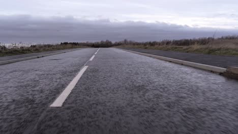 low angle flying above empty road markings - asphalt pavement long into distant horizon