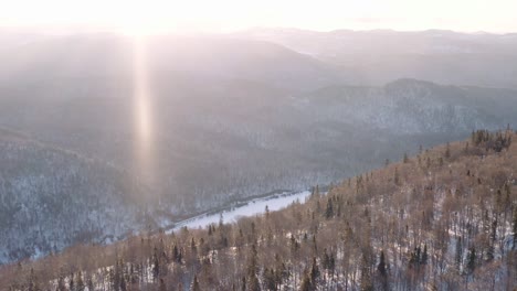 Dynamic-aerial-shot-of-snowy-river-and-valley-surrounded-by-boreal-forest-in-Parc-National-de-la-Jacques-Cartier,-Quebec-Canada