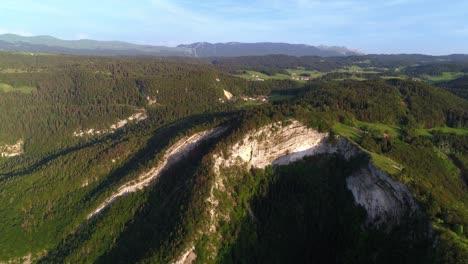 aerial flyover overgrown mountain of belvedere de la roche blanche and in background monts-jura during spring season and sunlight