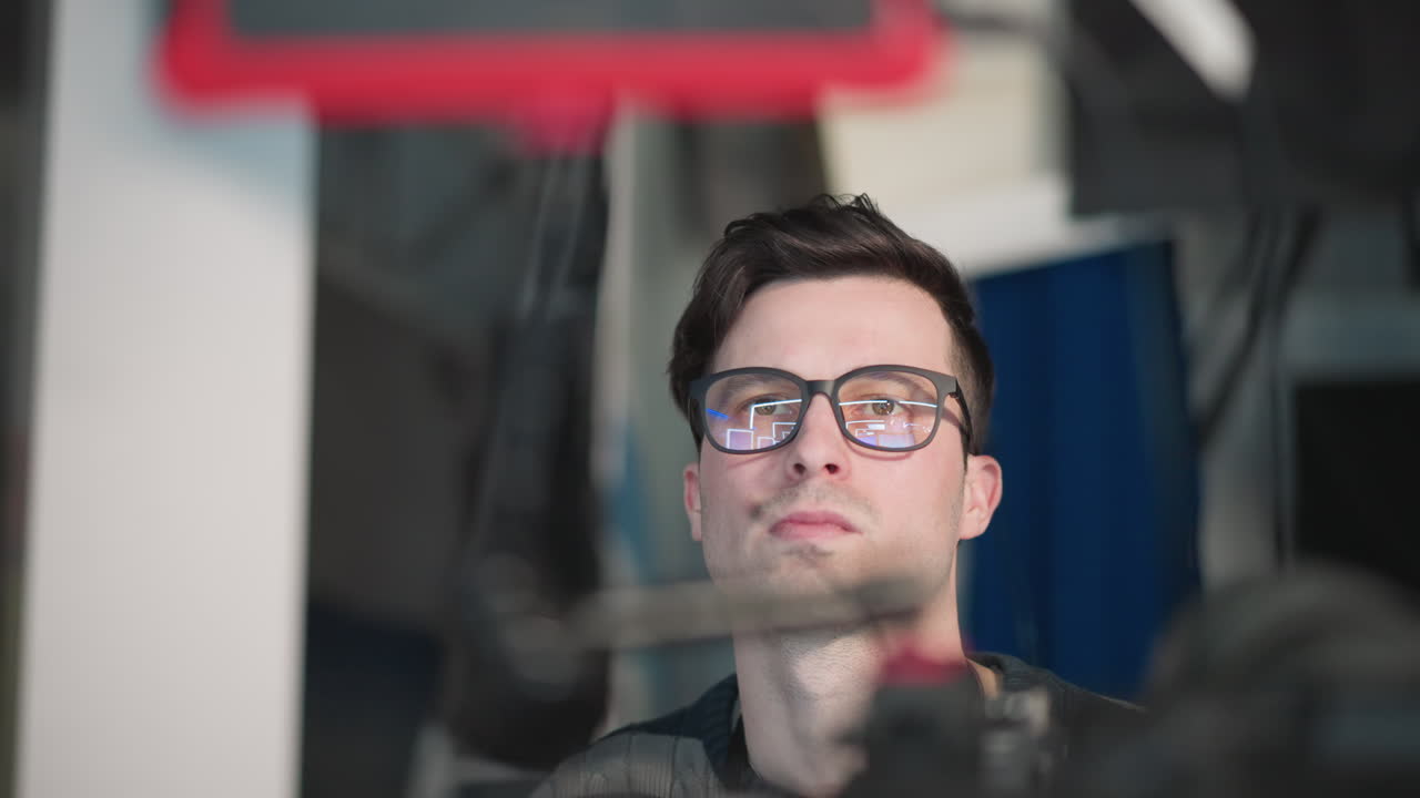 Close-up of camera operator focused while adjusting broadcast camera in professional studio. Reflections in glasses show camera and lighting setup, emphasizing attention to detail during filming