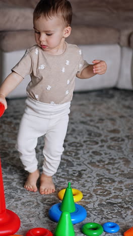 lovely baby boy takes a ring from pyramid. smart toddler assembling the toy in the room. vertical video