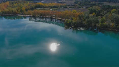 lake banyoles in autumn reflects blue sky, sun and trees, girona