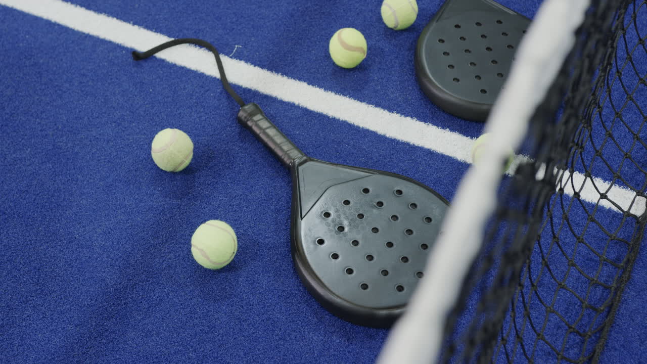 Racchette e palline da padel sparse su campo blu, pronte per la partita.