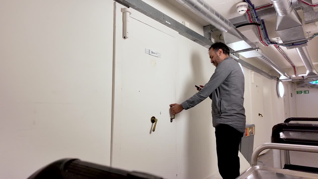 South Asian man opening a storage room door while holding a smartphone