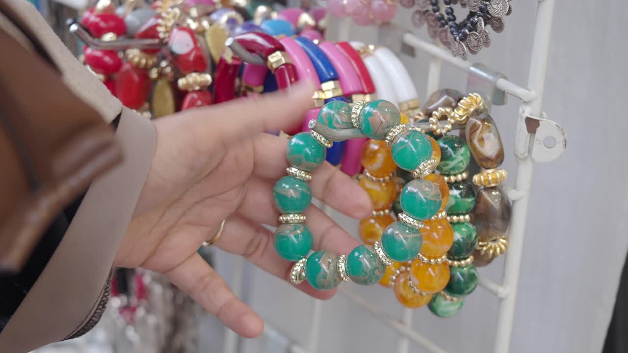 Primo piano di mano che esamina braccialetti di perline colorate a una bancarella del mercato