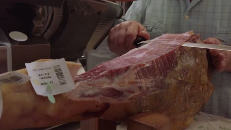 slow motion, spanish man cuts jamon iberico slices from leg of ham