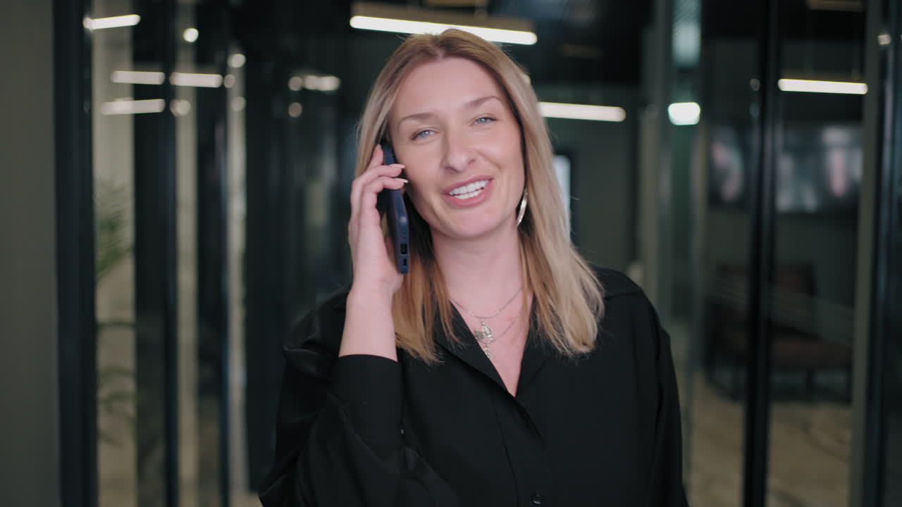 Smiling businesswoman looking on cellphone indoors. Surprised business woman reading message on mobile phone in office corridor. woman looking smartphone screen in business center. walking office
