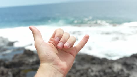 persona feliz muestra un gesto de mano fría mientras está de pie cerca de la costa rocosa de tenerife