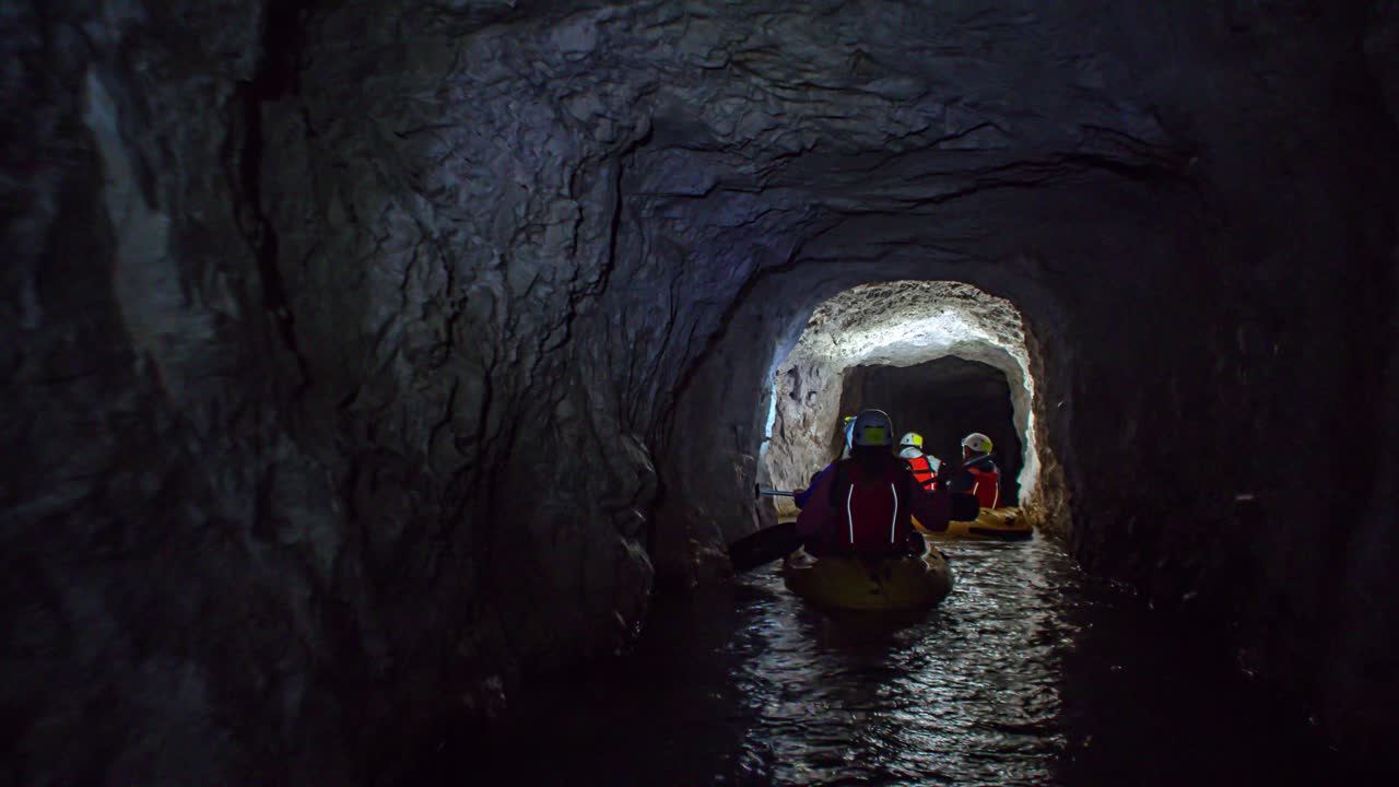 A group of people on boats entering a dark scary cave with a flashlight on the head