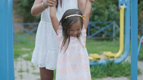 una madre embarazada y su hija joven disfrutan de un tiempo de juego juntos en un patio de recreo en el parque, rodeados de árboles y vegetación