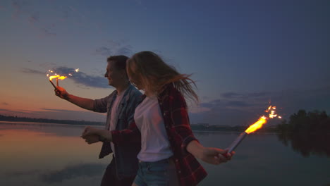 young lovers man and woman cheerfully run along the beach with hot sparkling rot in their hands in slow motion. romantic relationship. sparklers burn in the hands of lovers