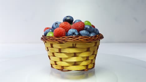 rotating wooden basket with different forest berries close-up on a white wooden table. 4k slow motion loop raw video with speed ramp effect.