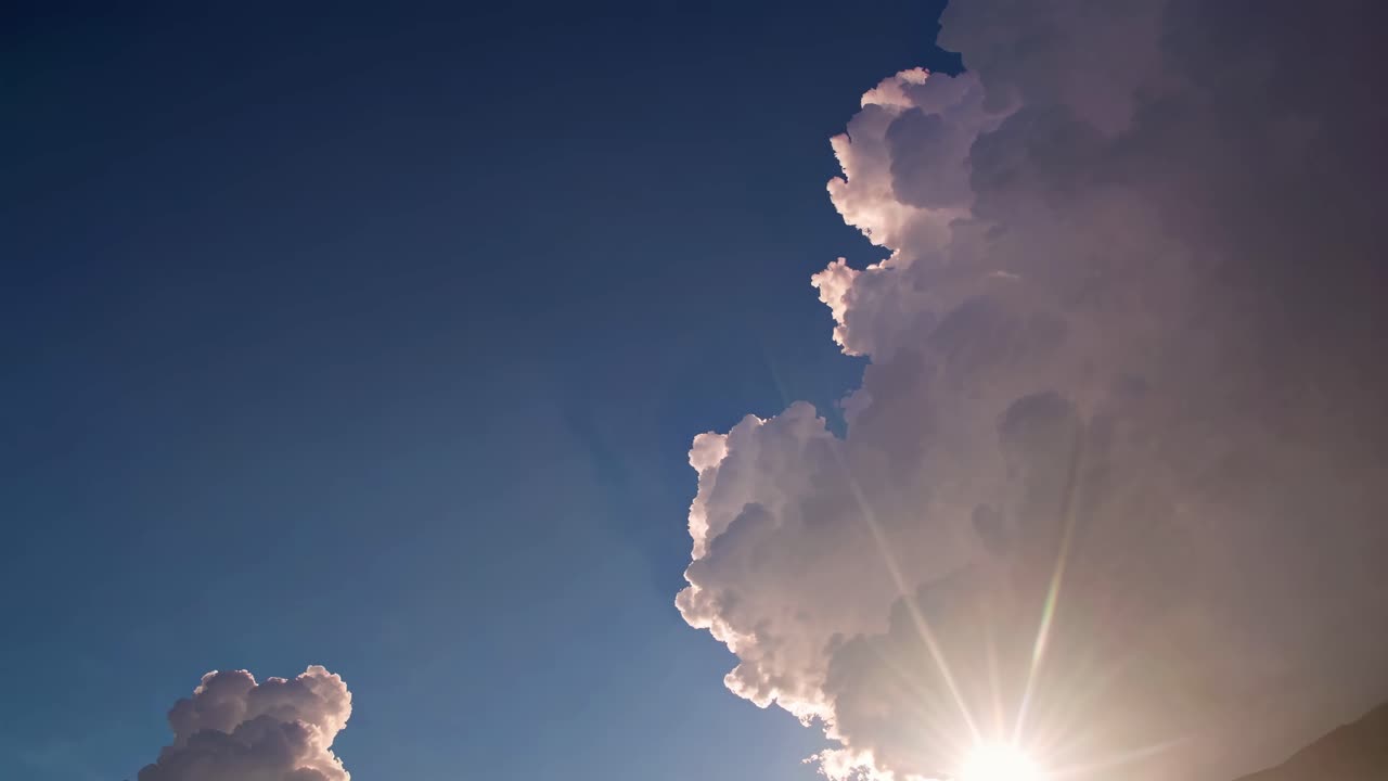 A low-angle video shot captures dramatic clouds with sunlight peeking through, set against a deep