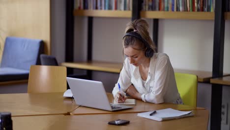 blonde woman study at distant learning at library, taking notes