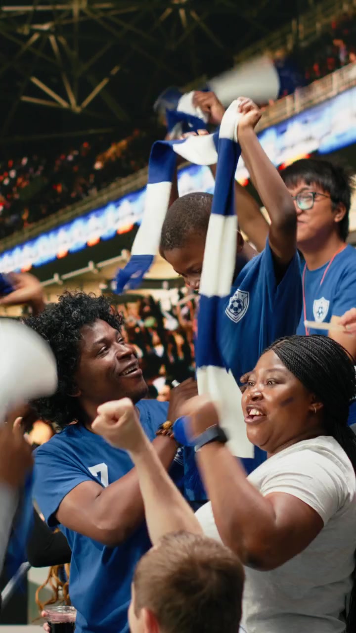 Video vertical. Joven aficionado al fútbol rodeado de felices seguidores del equipo azul animando.