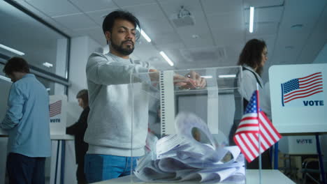 indian man puts ballot paper in box at polling station multicultural voters us people vote in voting booths at polling station indian man puts ballot paper in box national election day in the united states of america civic duty and patriotism concept