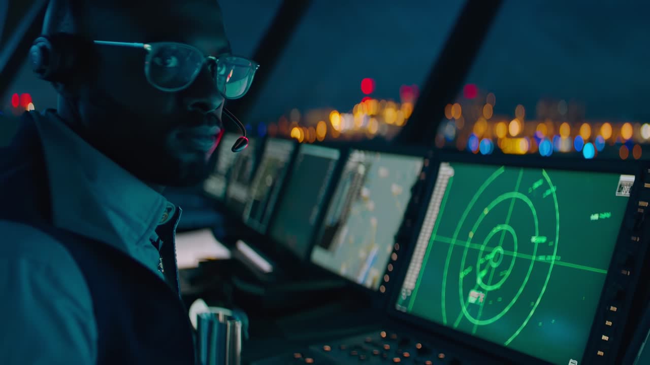 Side angle of a radar operator in a dimly lit control room, capturing a video of night operations