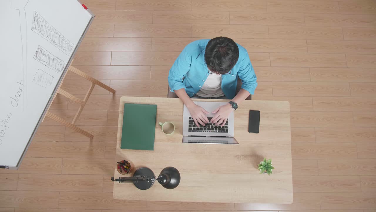 뷰  아웃 은 집에서 화이트보드 에 나무 책상에 앉아있는 동안 스마트폰 에 노트북에서 타이핑하는 성공을 축하하는 남자의 입니다.