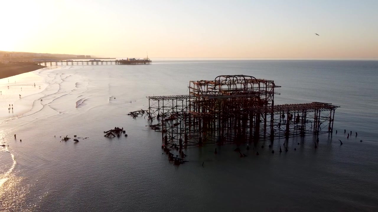 Drone shot panning backwards from the ruins of the West Pier as the sea and cityscape is revealed under the sunrise over the city