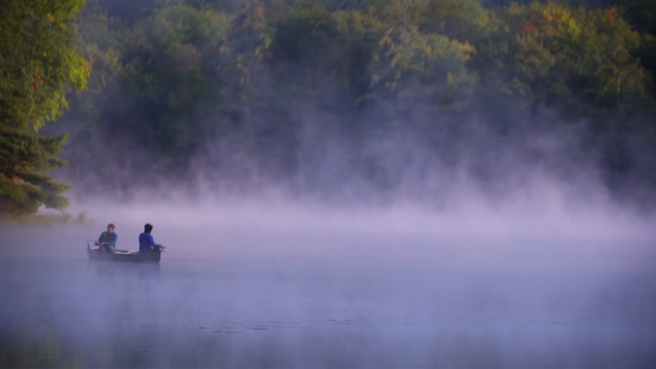 Fog floating over a pond on a misty morning with a fishing canoe