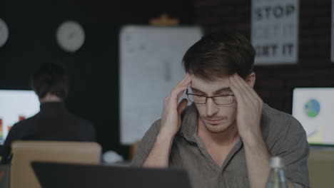 tired business man touching head in dark office. sad man working hard on laptop.