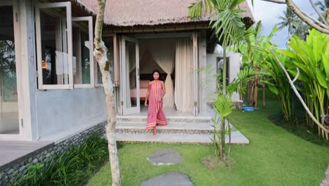 young asian girl in beautiful dress walking from villa entrance to outdoor garden on sunny morning in bali