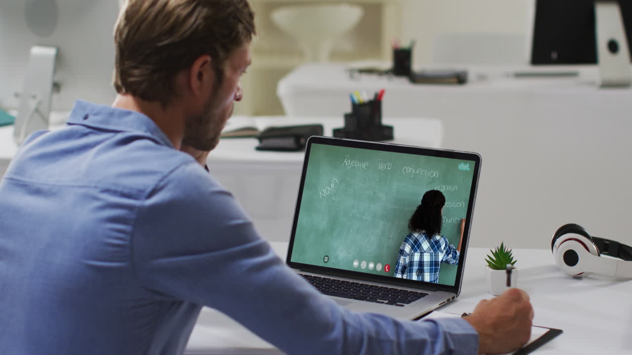 Caucasian male student using laptop on video call with female teacher, making notes