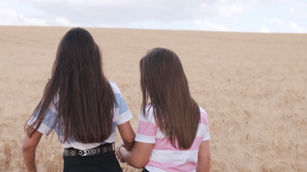 Two female friends holding hands and enjoying the day while walking together in a wheat field.