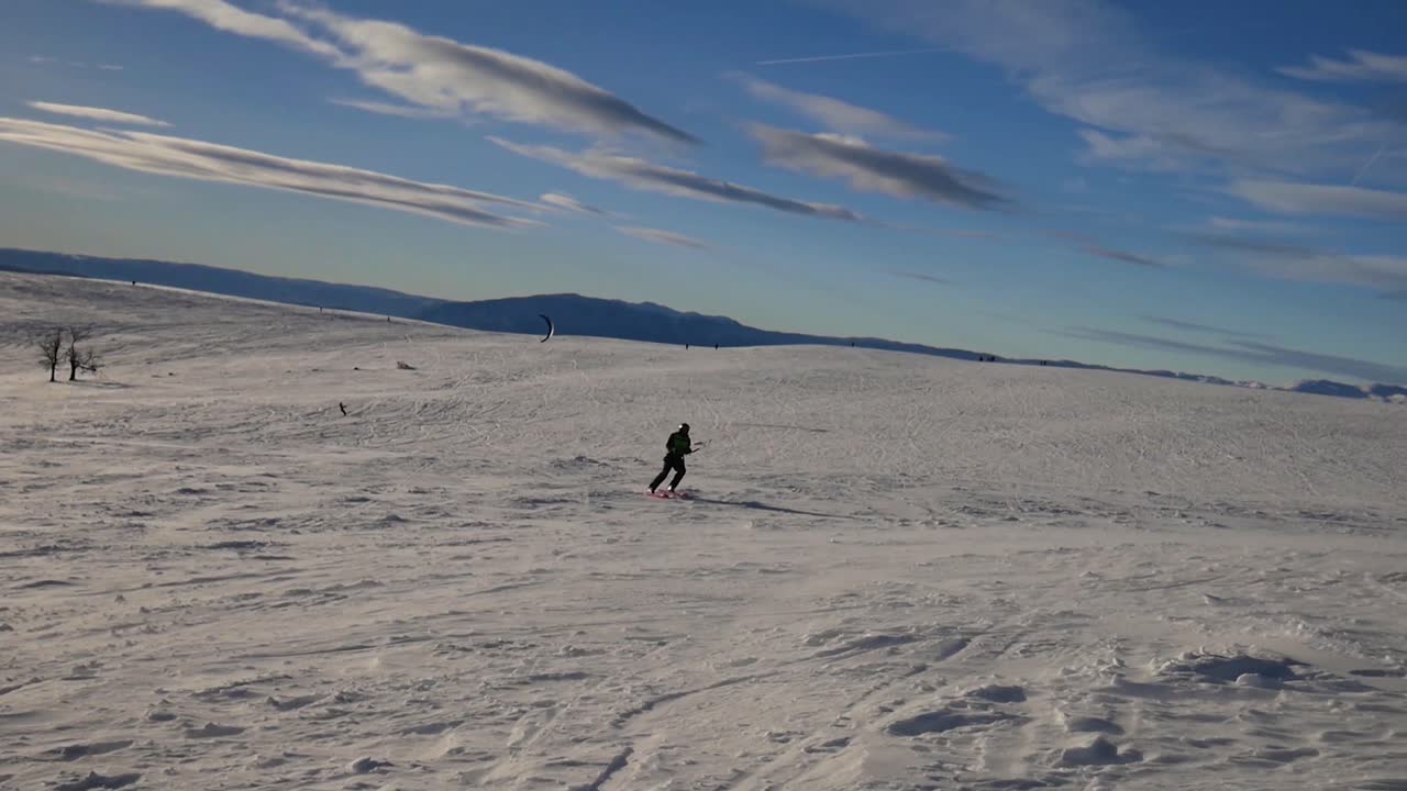 persona haciendo kite-ski hacia la cámara y girando en u en una llanura cubierta de nieve en los alpes franceses en un día despejado