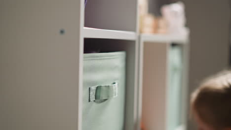 Little-girl-looks-inside-large-containers-on-wooden-rack