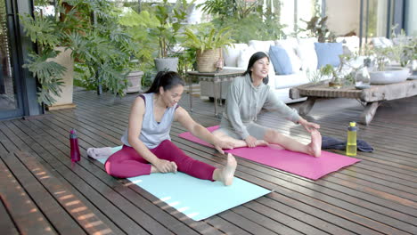 happy asian female friends stretching and smiling on sunny terrace, slow motion