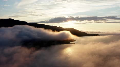 resplandor de la puesta de sol asomándose detrás de las montañas sobre nubes y olas -antena