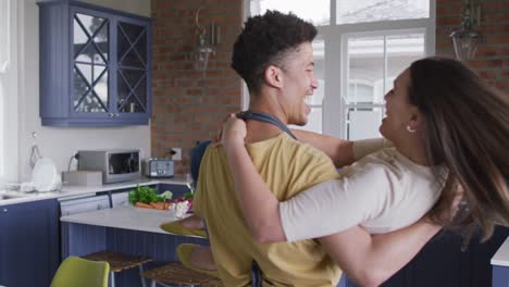 happy biracial couple embracing and laughing together in kitchen