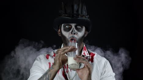 Creepy-man-with-skeleton-makeup-in-white-shirt.-Guy-looking-at-camera,-drinks-milk-from-a-glass